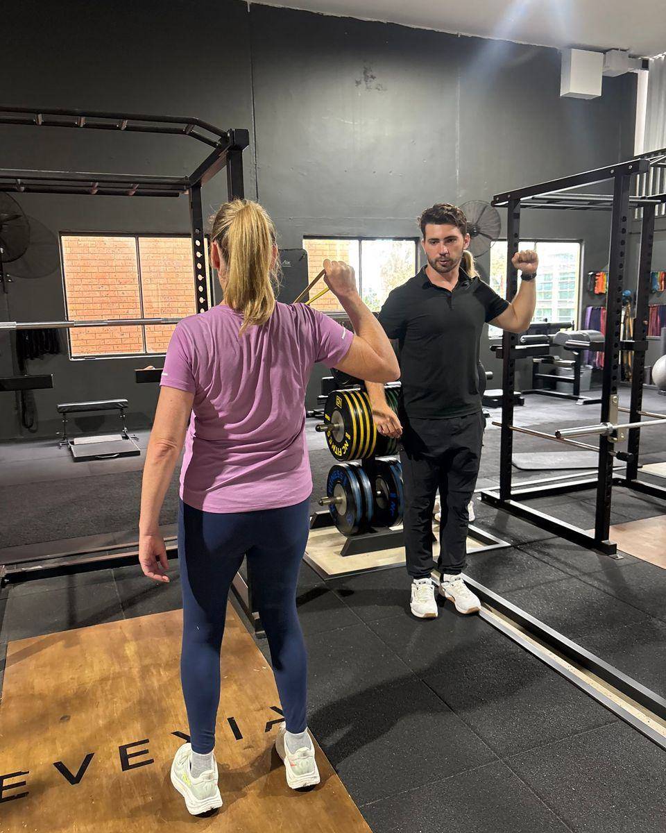 1-on-1 Personal Trainer Northern Beaches — Solve PT Max demonstrating a banded shoulder rotation for a client in a 1-on-1 session