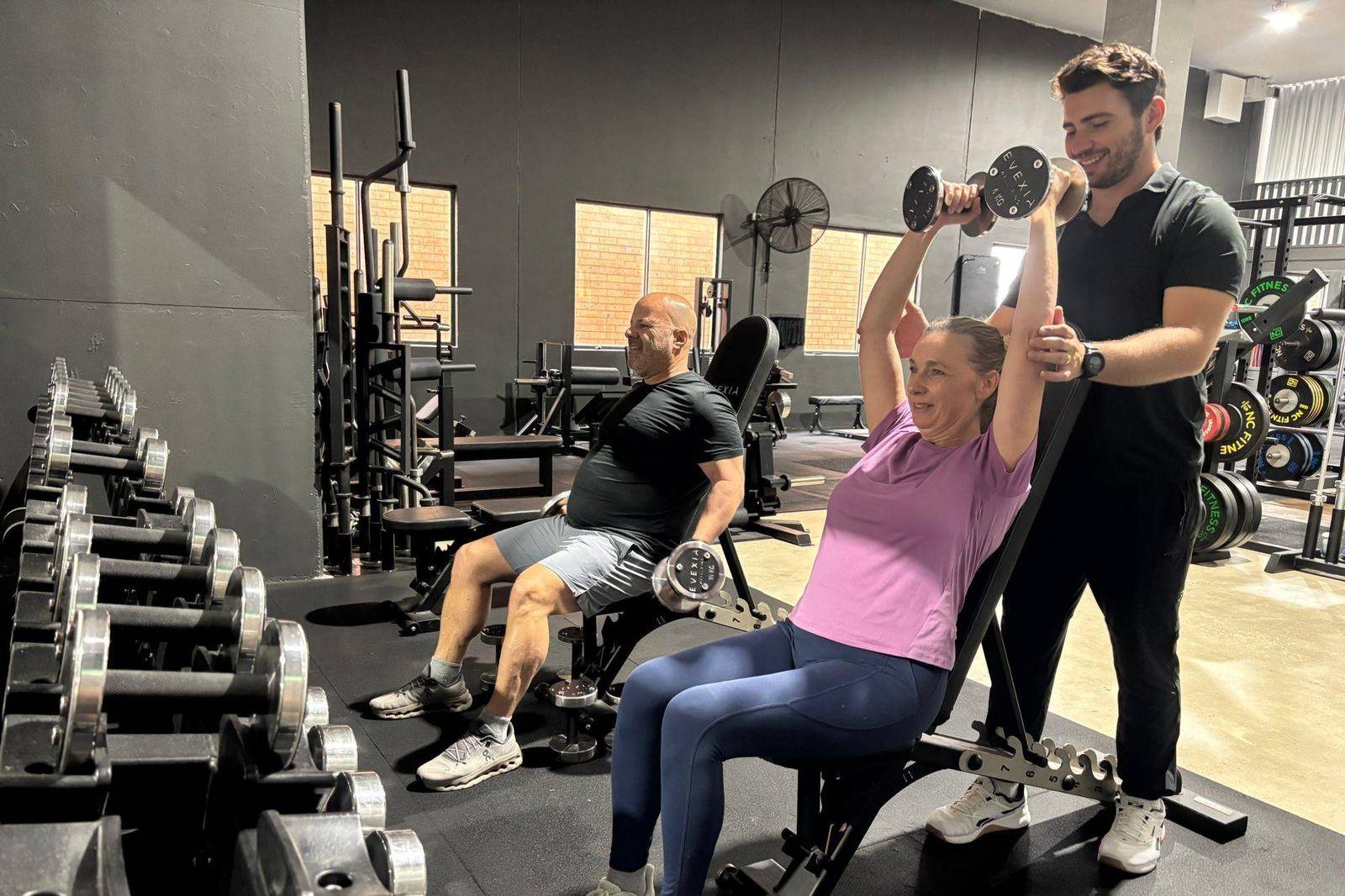 Max coaching a client through an overhead dumbbell press while another client trains alongside, Solve Personal Training, Brookvale
