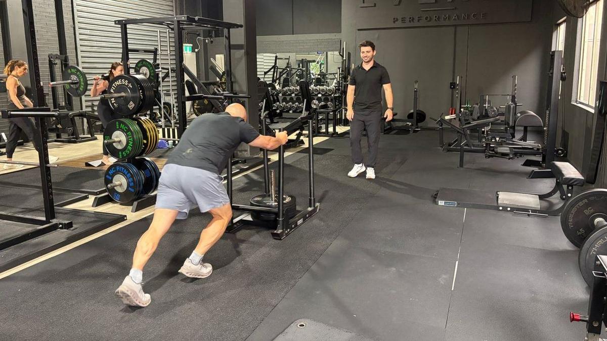 Small Group Training Northern Beaches — Solve PT A client pushing the sled while Max coaches, with other clients training in the background